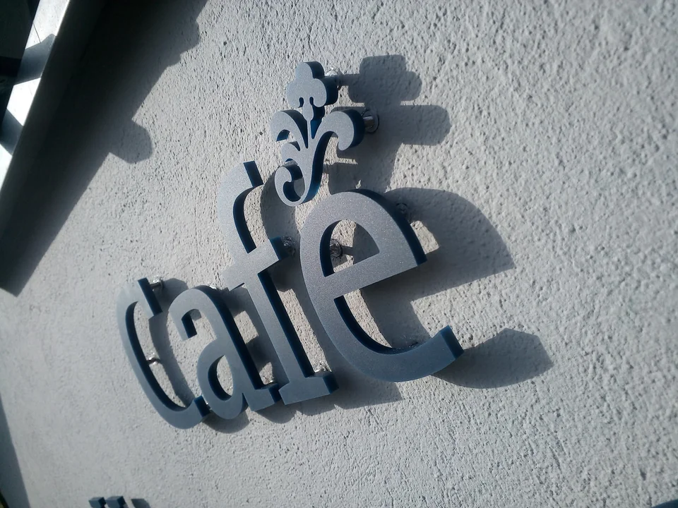 Dunkler dreidimensionaler Café-Schriftzug an einer hellen Putzfassade