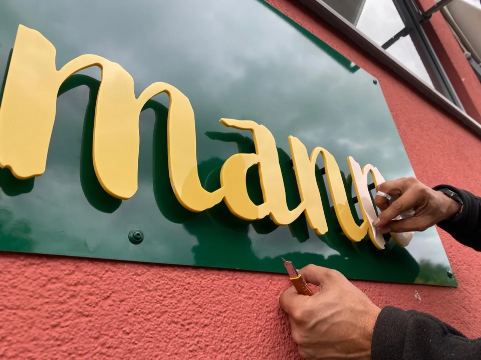 Montage gelber Einzelbuchstaben auf einem grünen Schild an einer roten Fassade