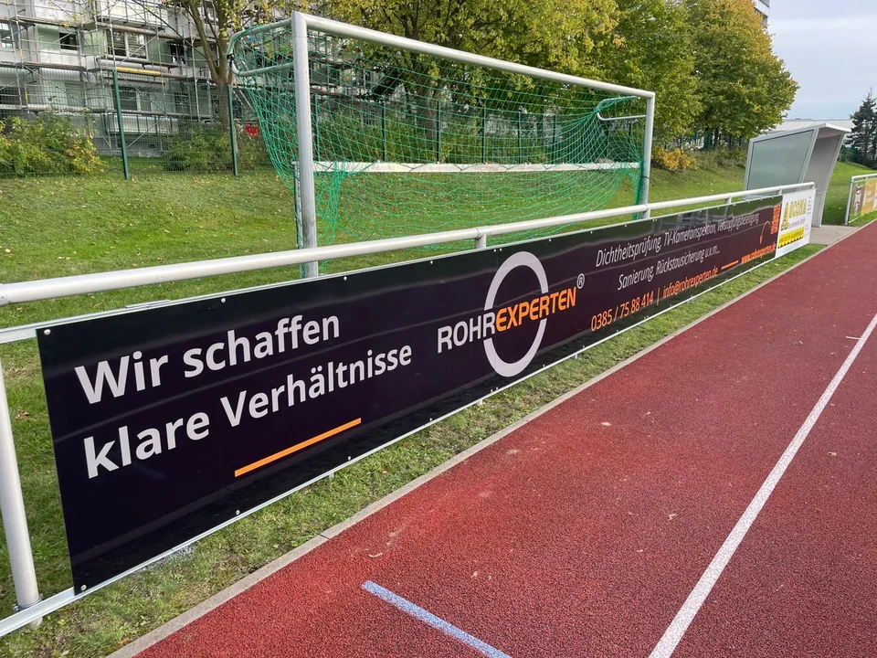 Schwarze Bandenwerbung der Rohrexperten an einem Sportplatz