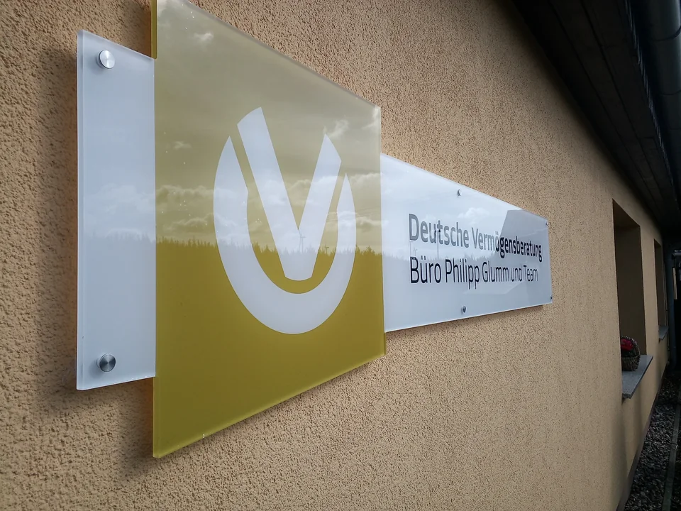 Mehrteiliges Firmenschild der Deutschen Vermögensberatung mit goldfarbenem Logo an einer Hauswand