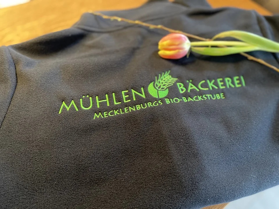 Grünes Logo der Mühlenbäckerei als Stickerei auf grauem Fleece