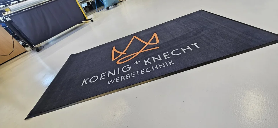Dunkle Fußmatte mit orange-weißem KOENIG+KNECHT-Logo