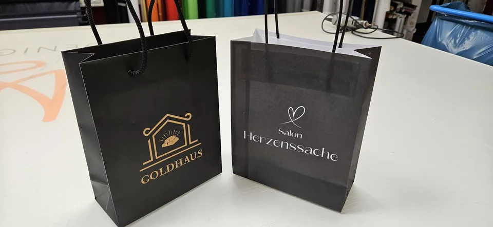 Schwarze Papiertaschen mit Logos von Goldhaus und Salon Herzenssache